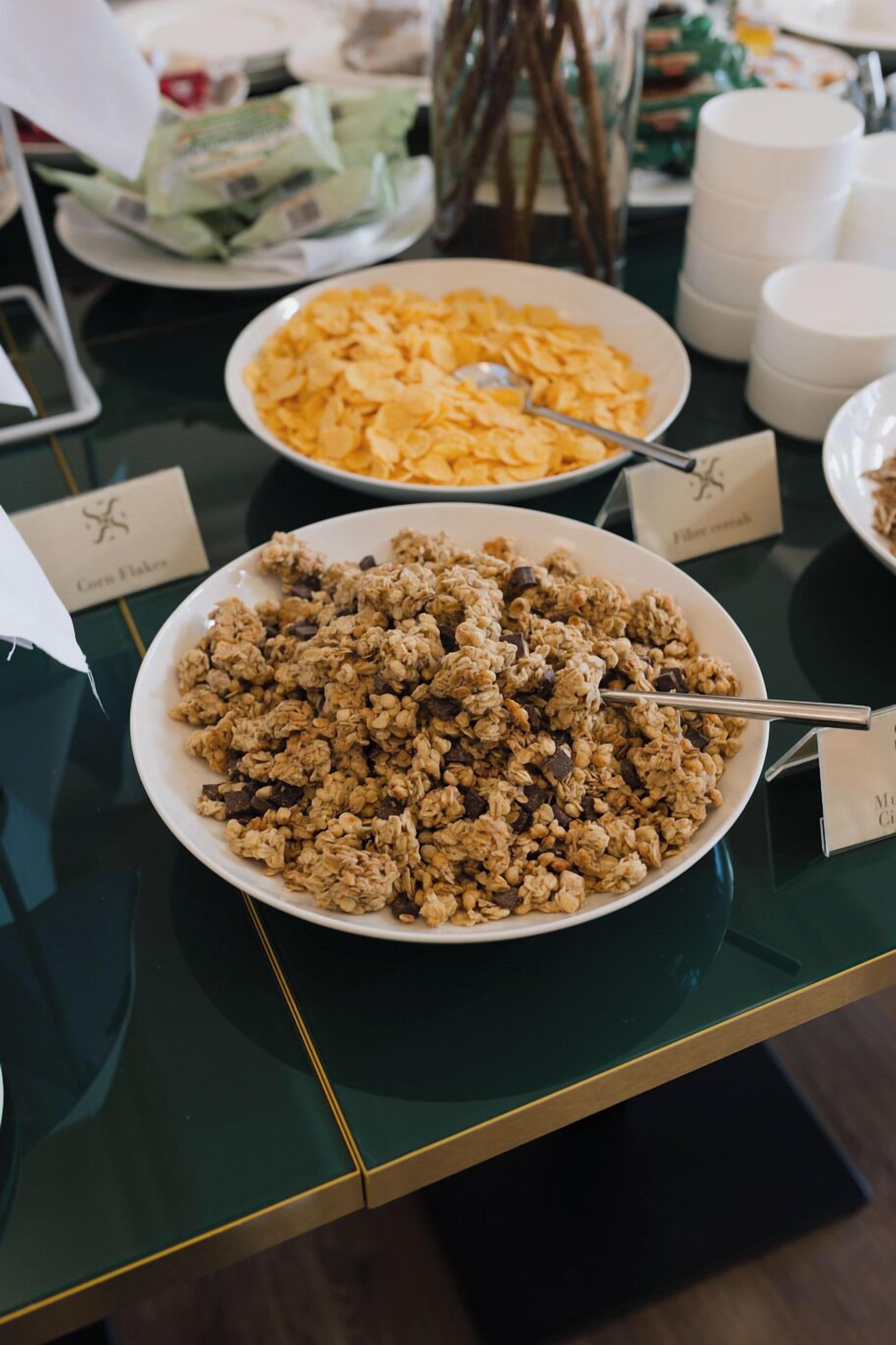 A buffet table with various dishes including cereal and granola.