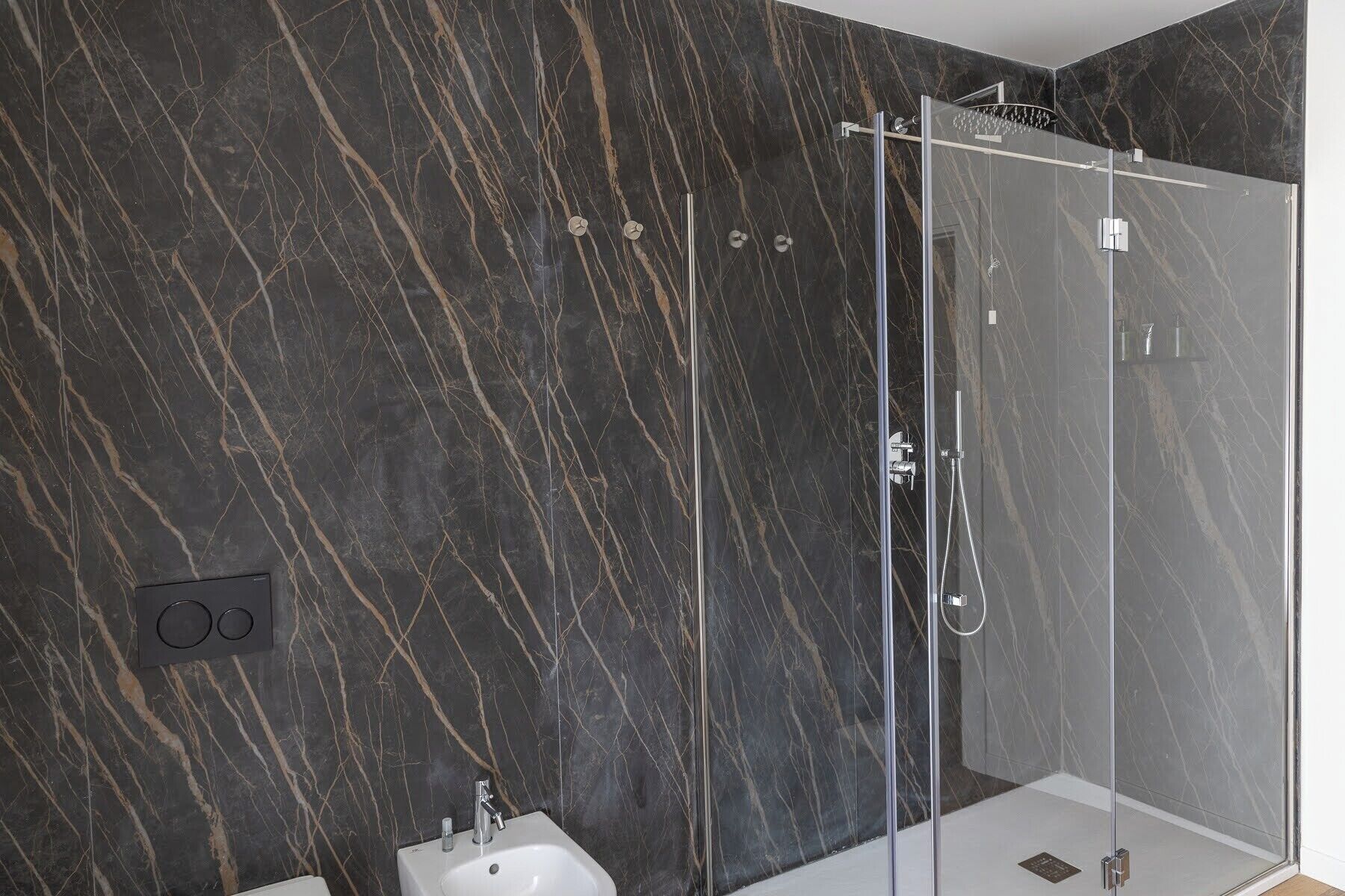 Un bagno moderno con doccia vetrata, pareti in marmo e lavandino bianco.