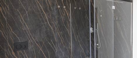 A modern bathroom with a glass-enclosed shower, marble walls, and a white sink.