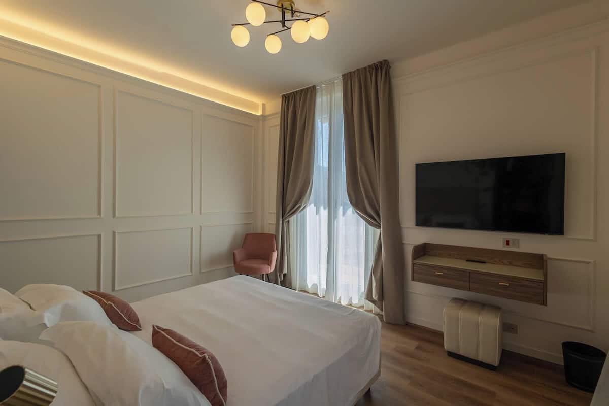 Ein Hotelzimmer mit einem großen Bett, einem an der Wand befestigten Fernseher, einer Holzkommode und einem Sessel.