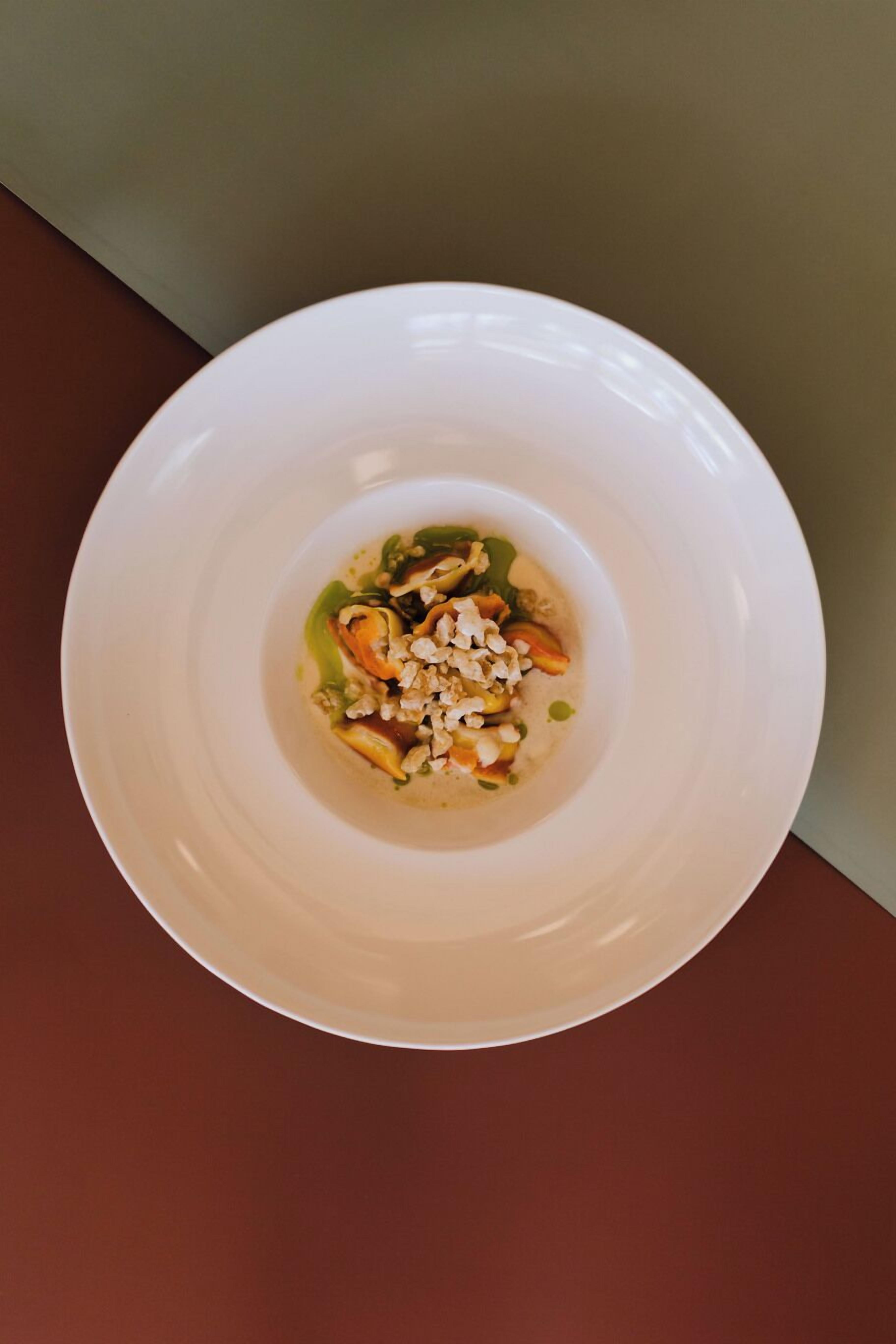 A white plate with a dish containing vegetables and nuts on a brown surface.