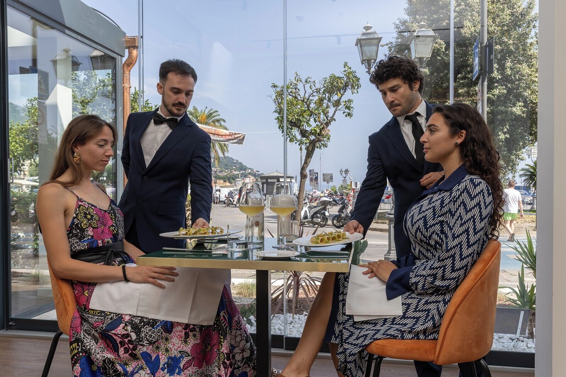 Un espace repas avec une table dressée pour quatre personnes, une vue sur la rue et des sièges à l’extérieur.
