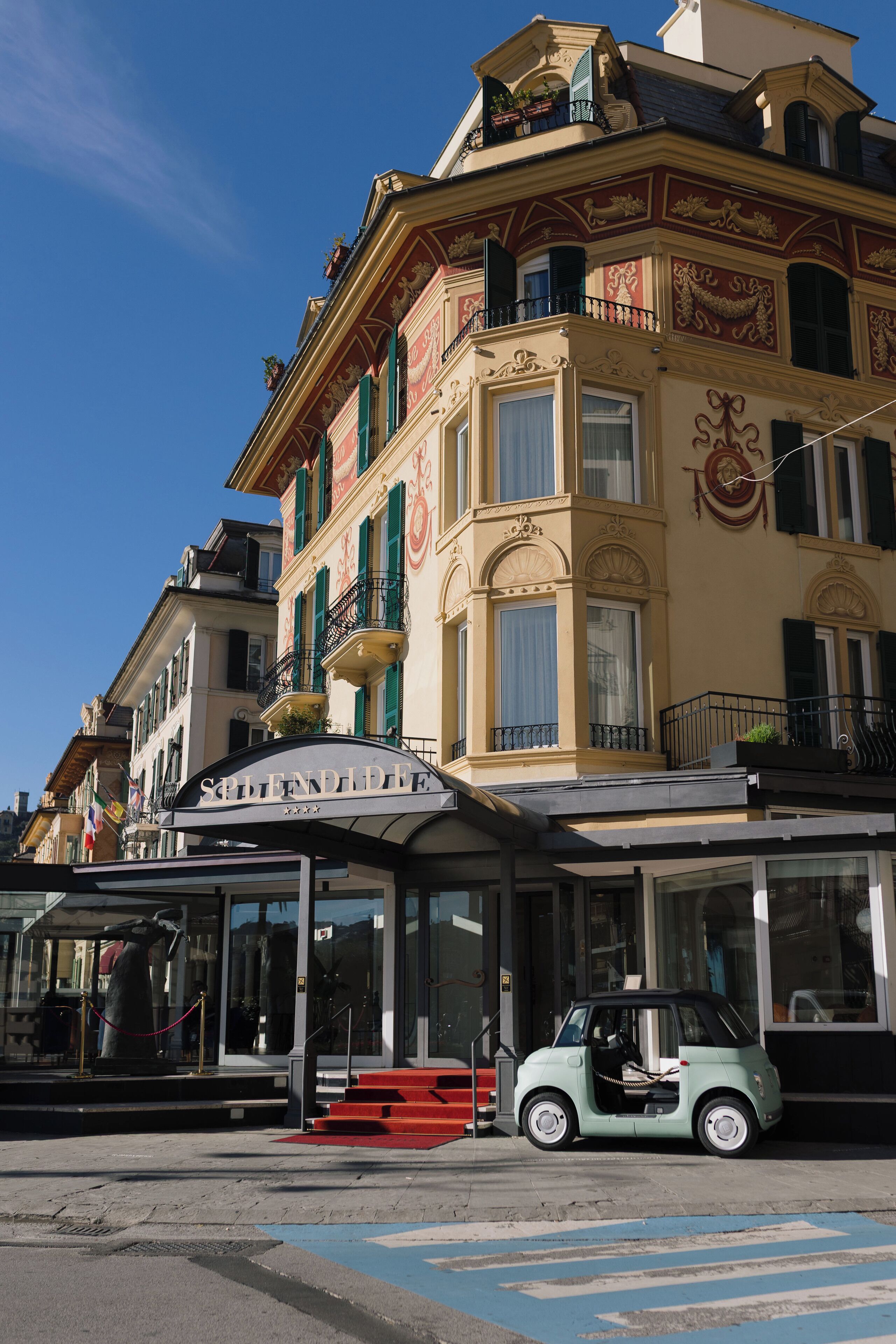 Un edificio con un cartel que dice "Splendid Hotel" y un pequeño coche verde estacionado adelante.
