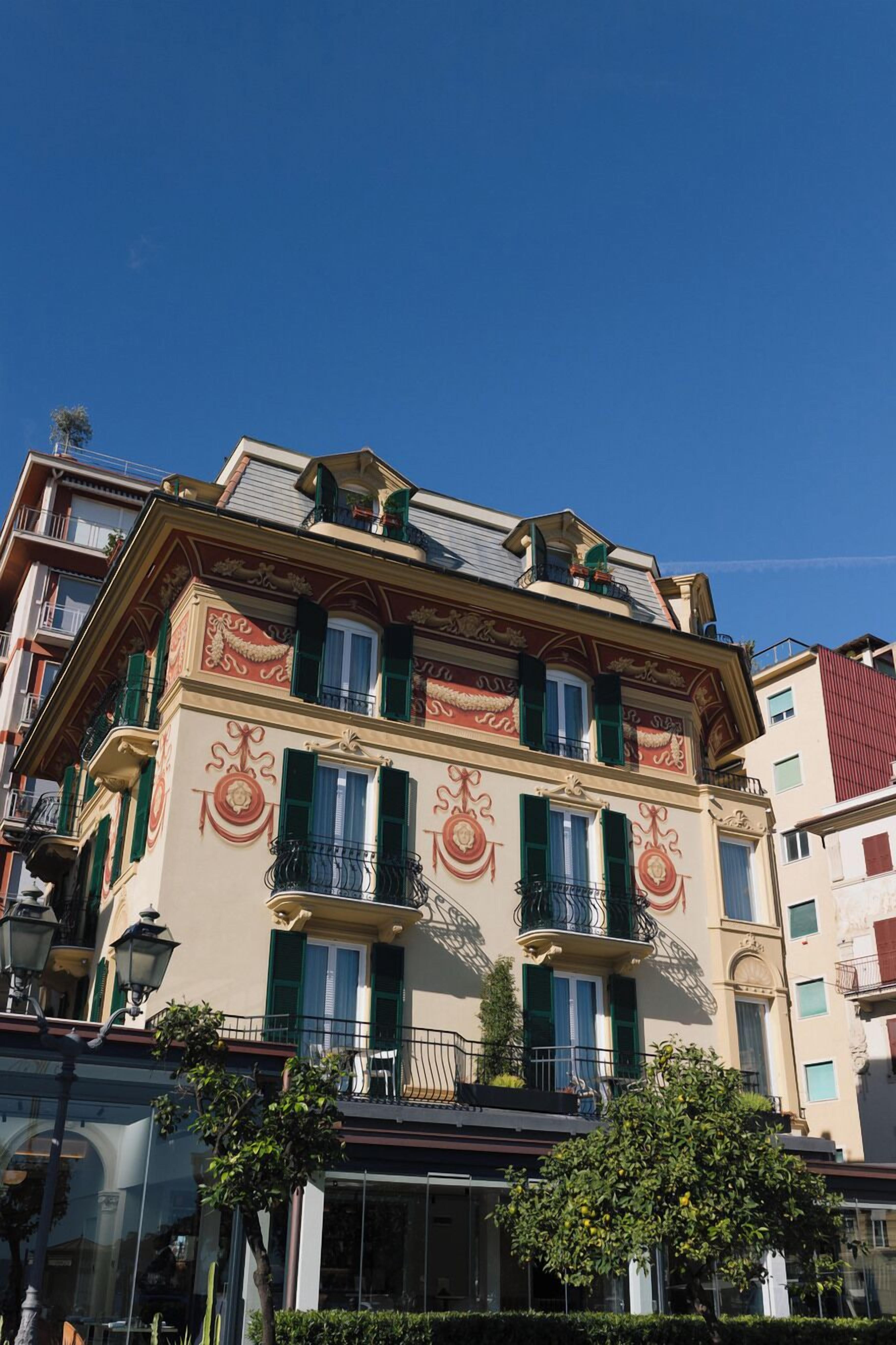 Un immeuble à plusieurs étages, doté de détails architecturaux raffinés, de volets verts et de balcons.