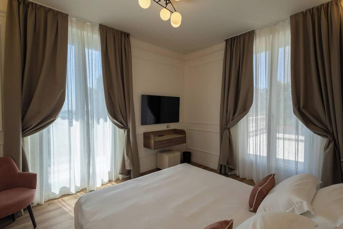 Ein Hotelzimmer mit einem großen Bett, einem an der Wand befestigten Fernseher und einem Nachttisch aus Holz.