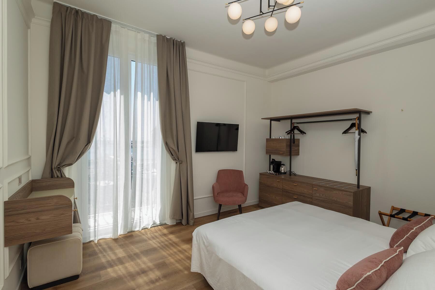 A hotel room with a bed, a desk, a chair, a television, and a wardrobe.