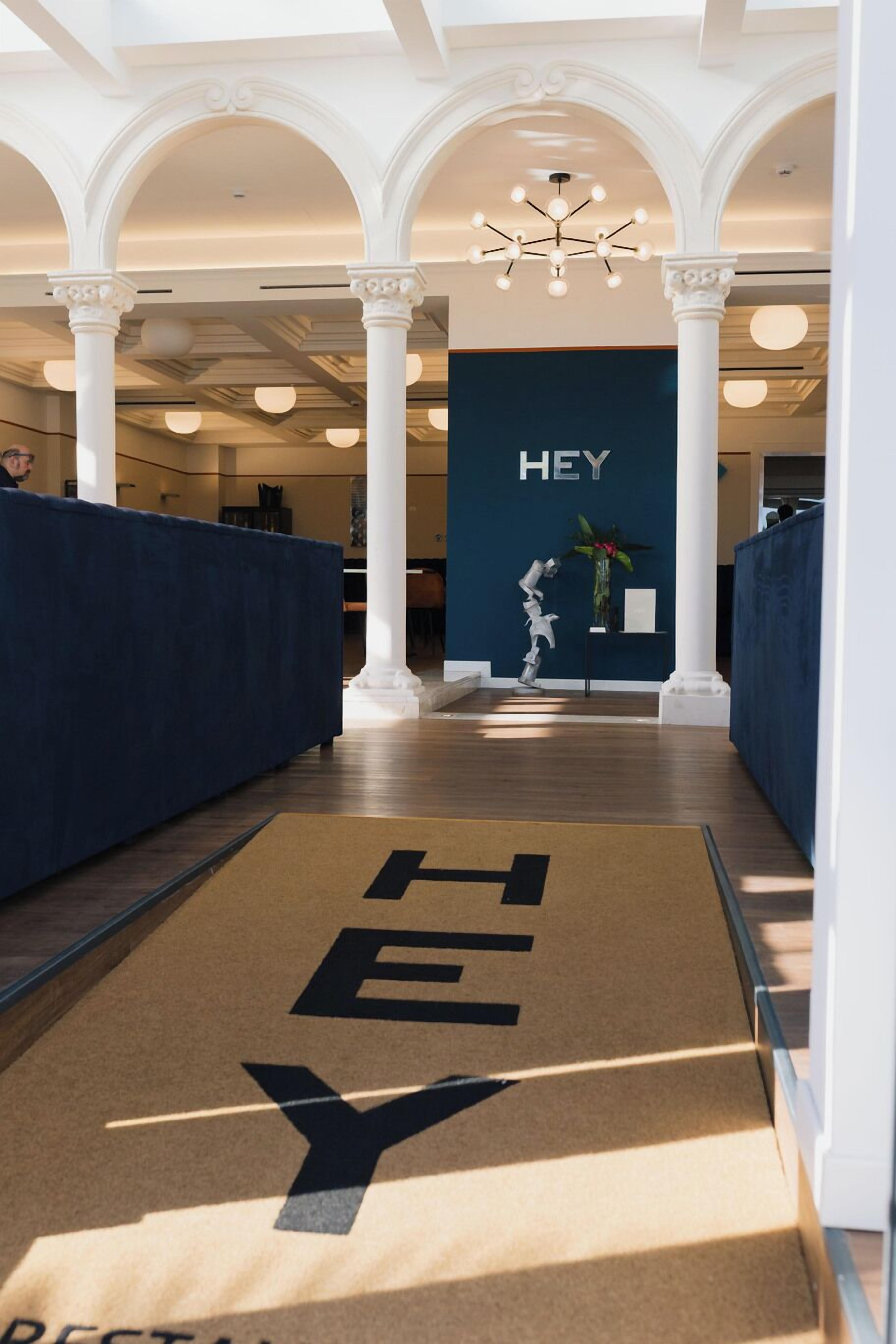 Una hall d'albergo con una reception, un cartello con la scritta 'HEY' sul muro e un tappetino con il simbolo 'Y'.