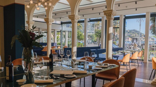 A restaurant with a long table set for dining, large windows offering a view of the city, and a decorative plant centerpiece. - SPLENDIDE RIVIERA   (Rapallo)
