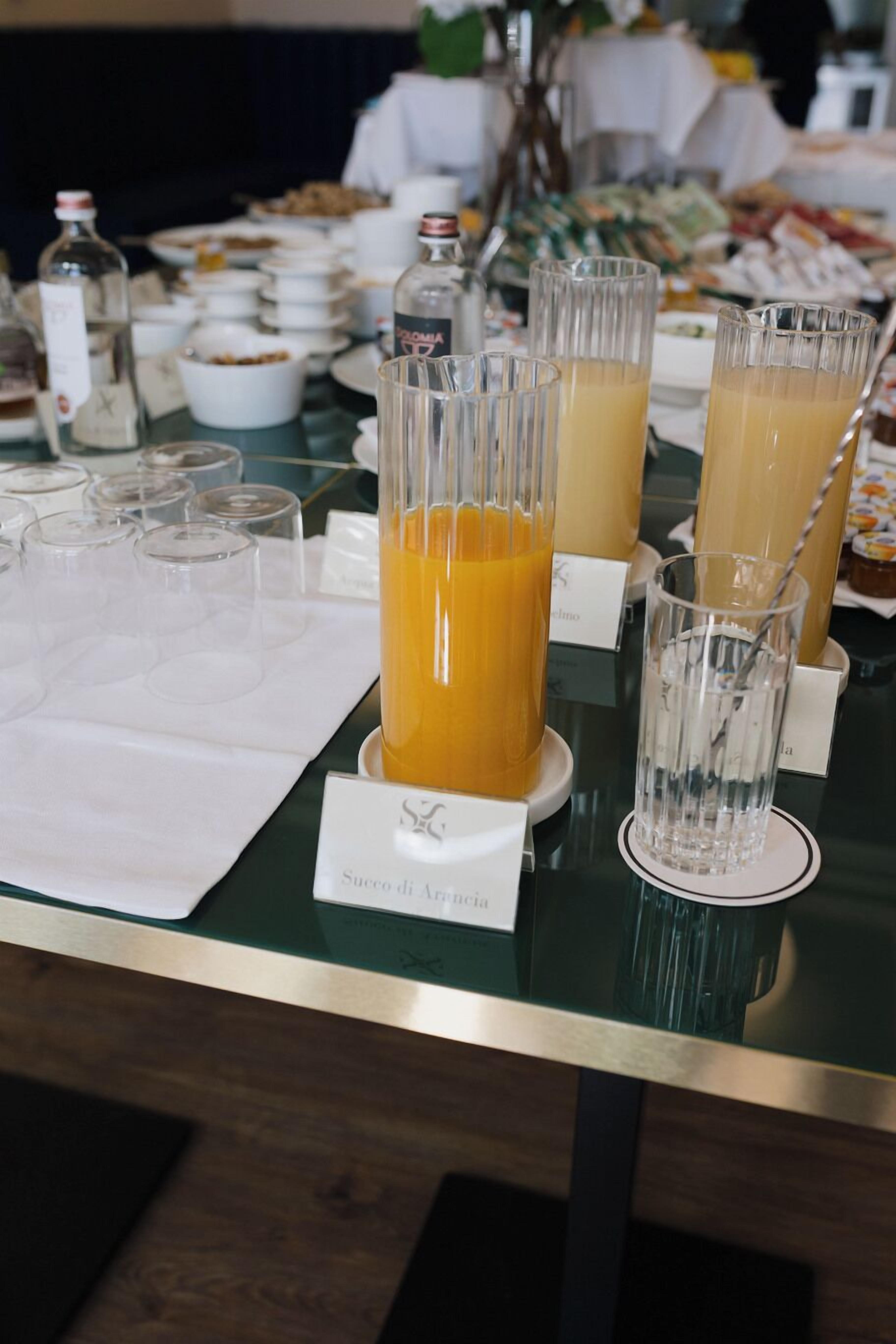 Une table de buffet proposant divers plats et boissons, notamment du jus d’orange et de l’eau.