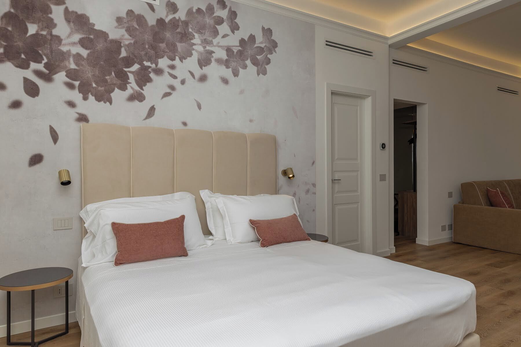Camera da letto con un letto grande, due comodini, una lampada a parete e una porta che dà su un'altra stanza.