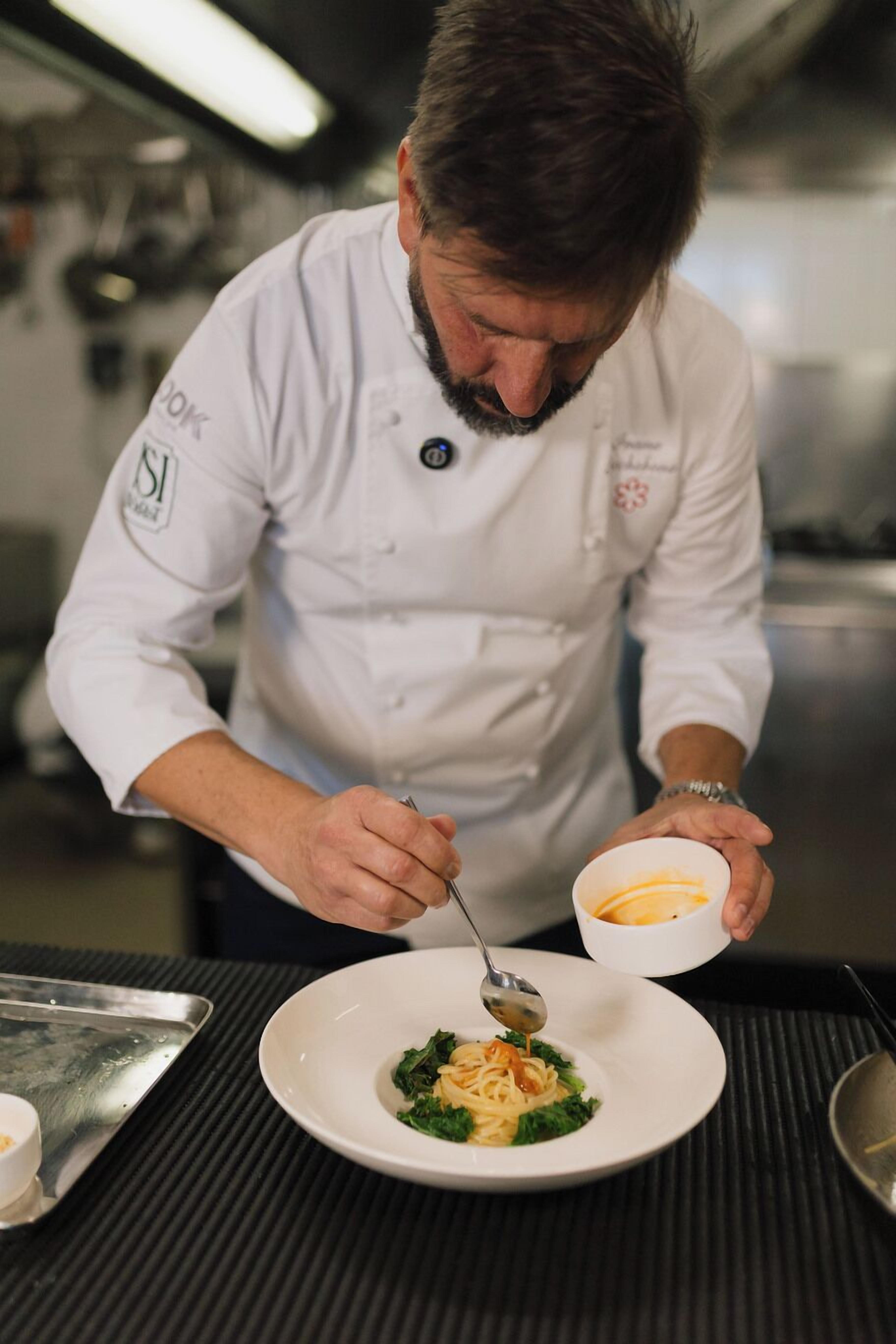 Um chef com uniforme branco preparando um prato com uma colher e uma tigela.