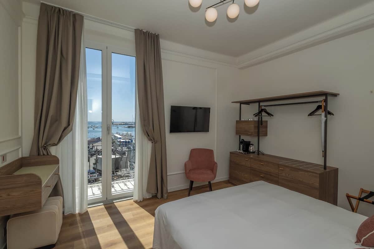 Ein Hotelzimmer mit Bett, Schreibtisch, Stuhl, Fernseher und Blick auf die Stadt durch große Fenster.