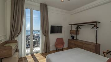 Une chambre d’hôtel équipée d’un lit, d’un bureau, d’une chaise, d’une télévision et offrant une vue sur la ville grâce à de grandes fenêtres.