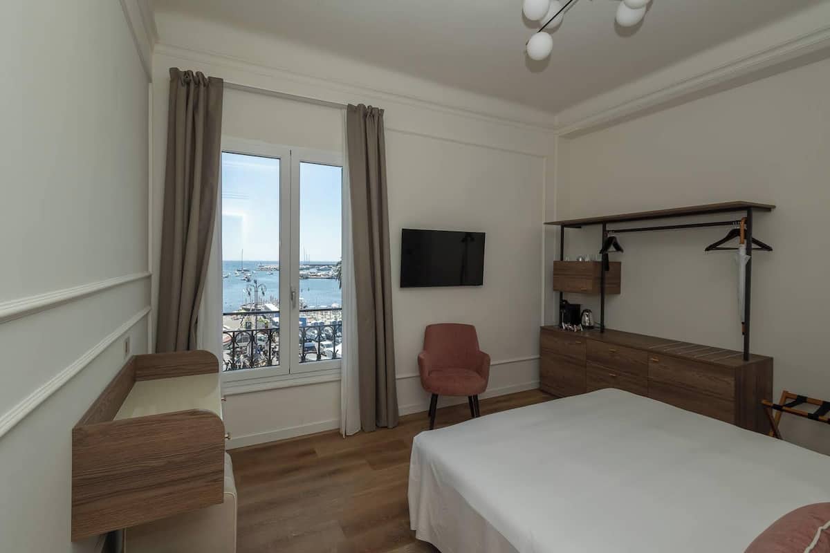 Ein Hotelzimmer mit Balkon, einem Bett, einem Schreibtisch, einem Sessel, einem Fernseher und einem Kleiderschrank.