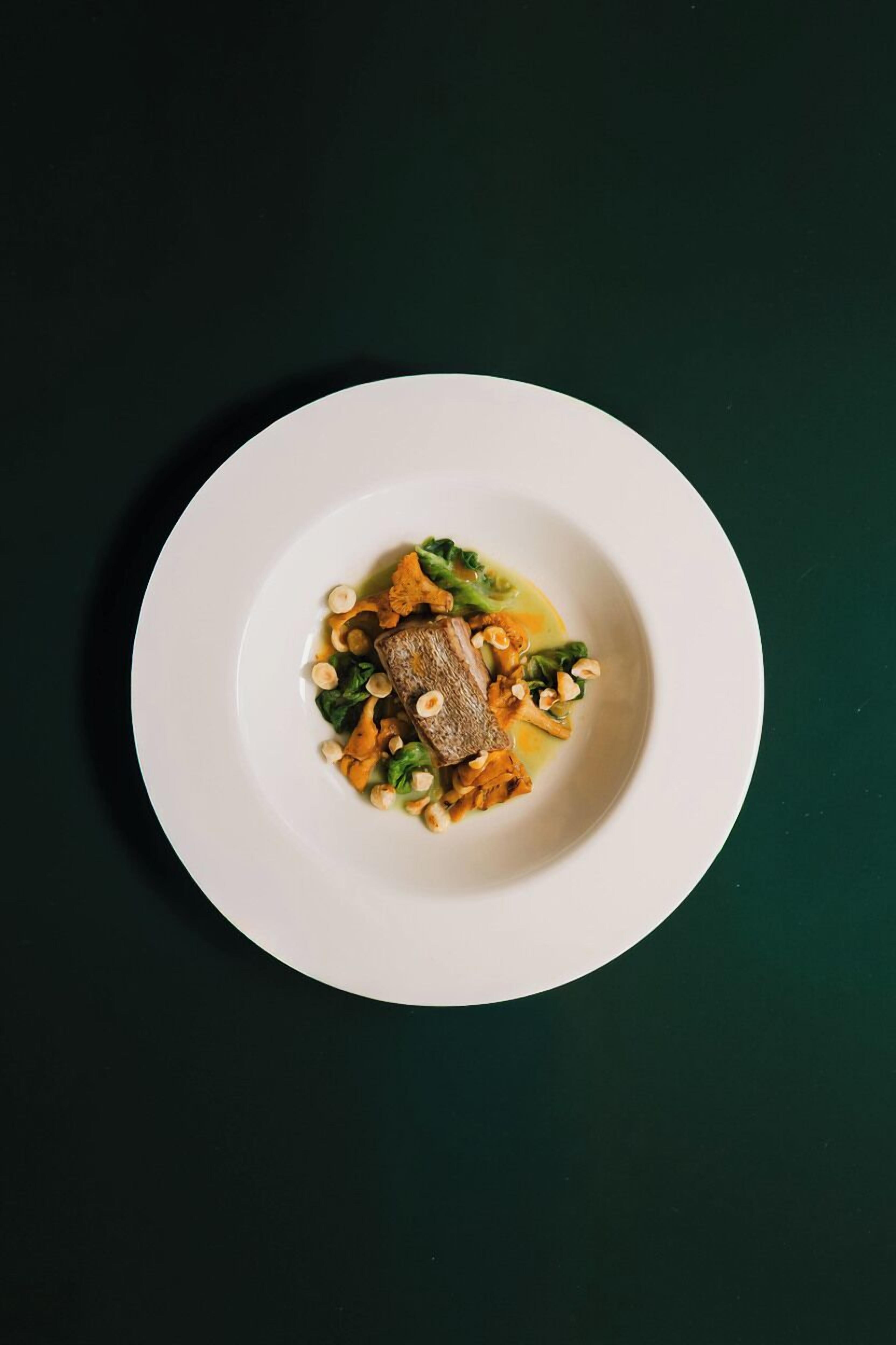 A white plate with a piece of meat, vegetables, and a sauce on a dark surface.