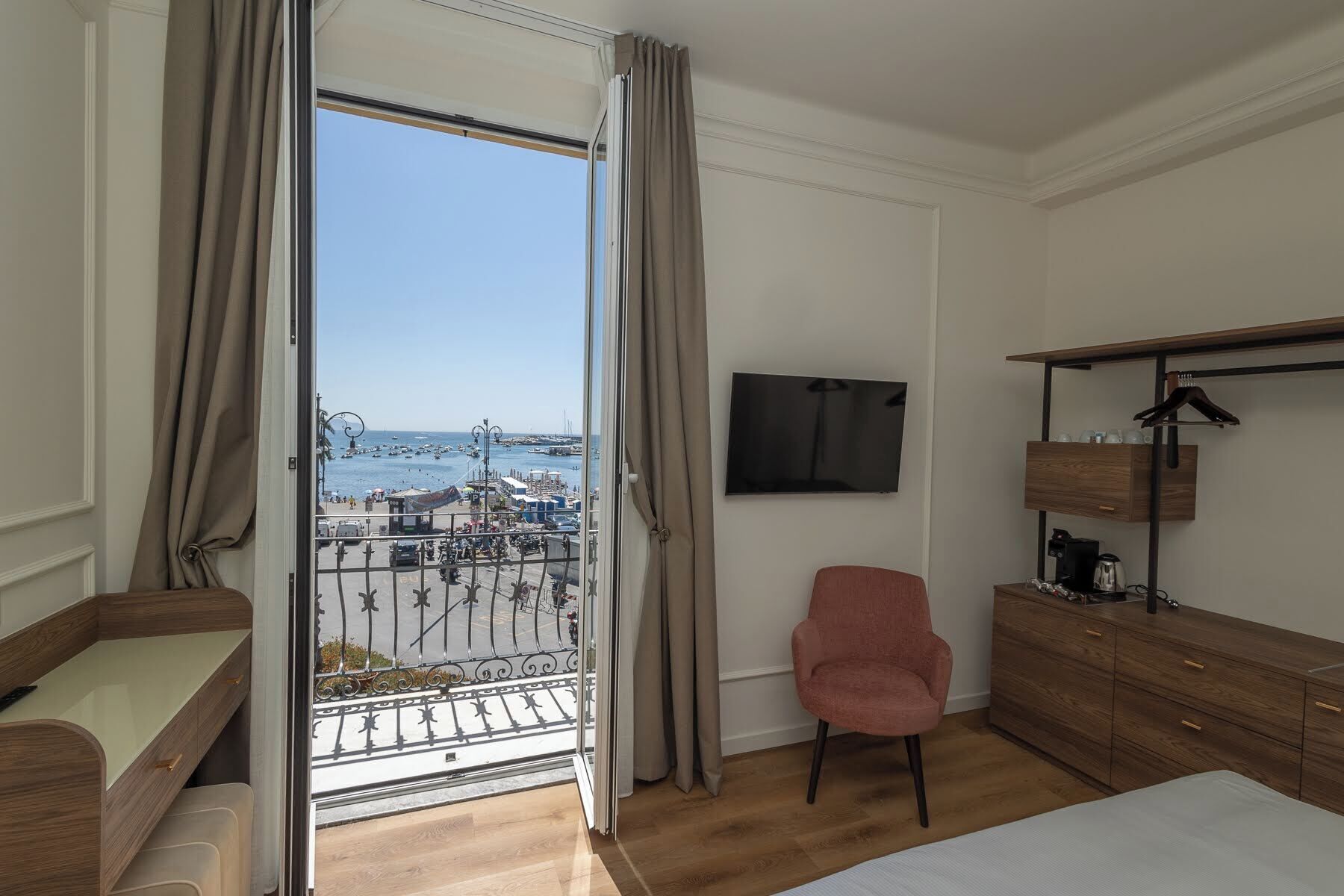 A hotel room with a balcony, a TV, a desk, a chair, and a wardrobe.