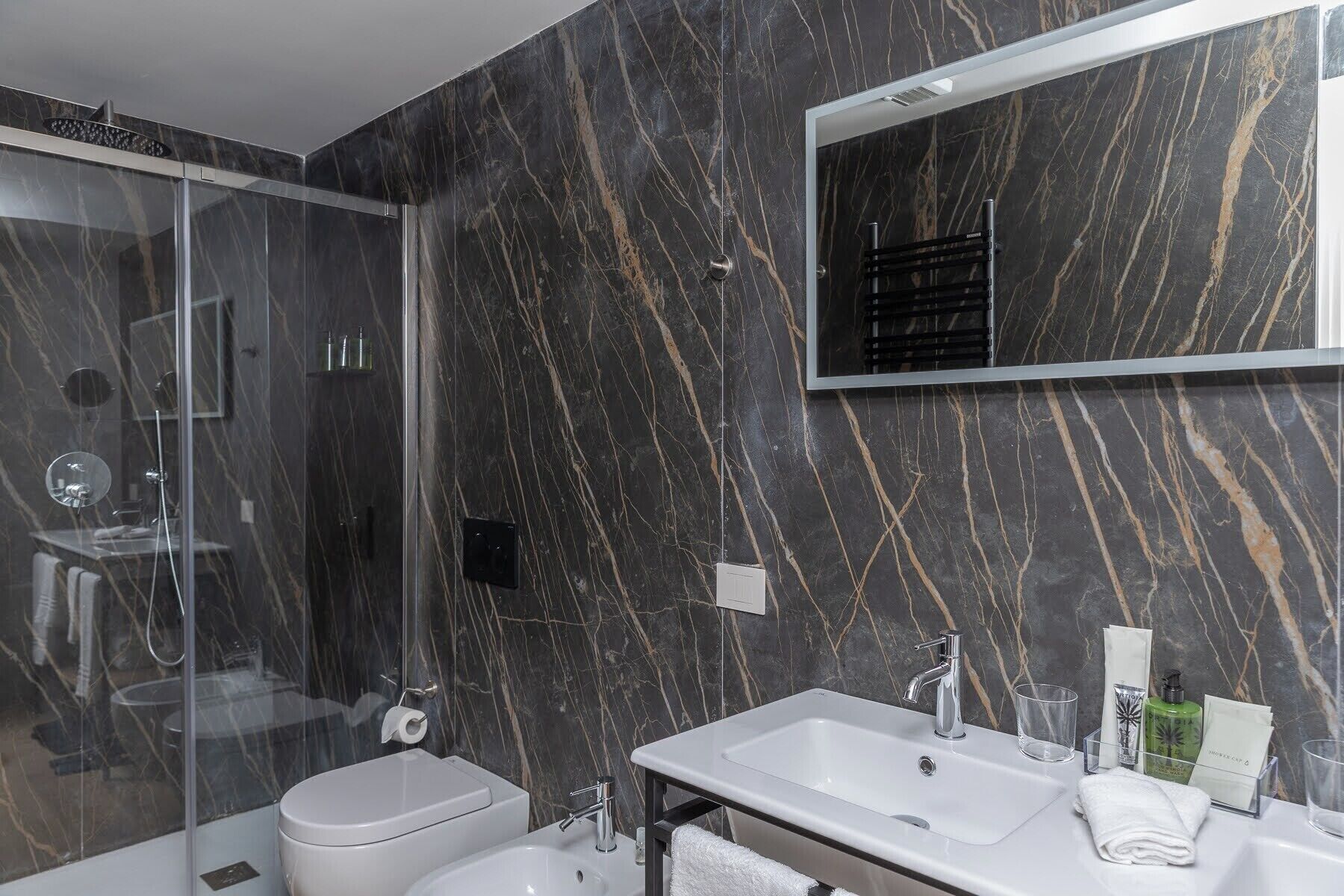 Un baño moderno con ducha de vidrio, inodoro blanco, lavamanos con espejo y artículos de aseo en la encimera.