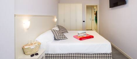 A neatly made bed with patterned pillows, a bedside basket, and a red tray.
