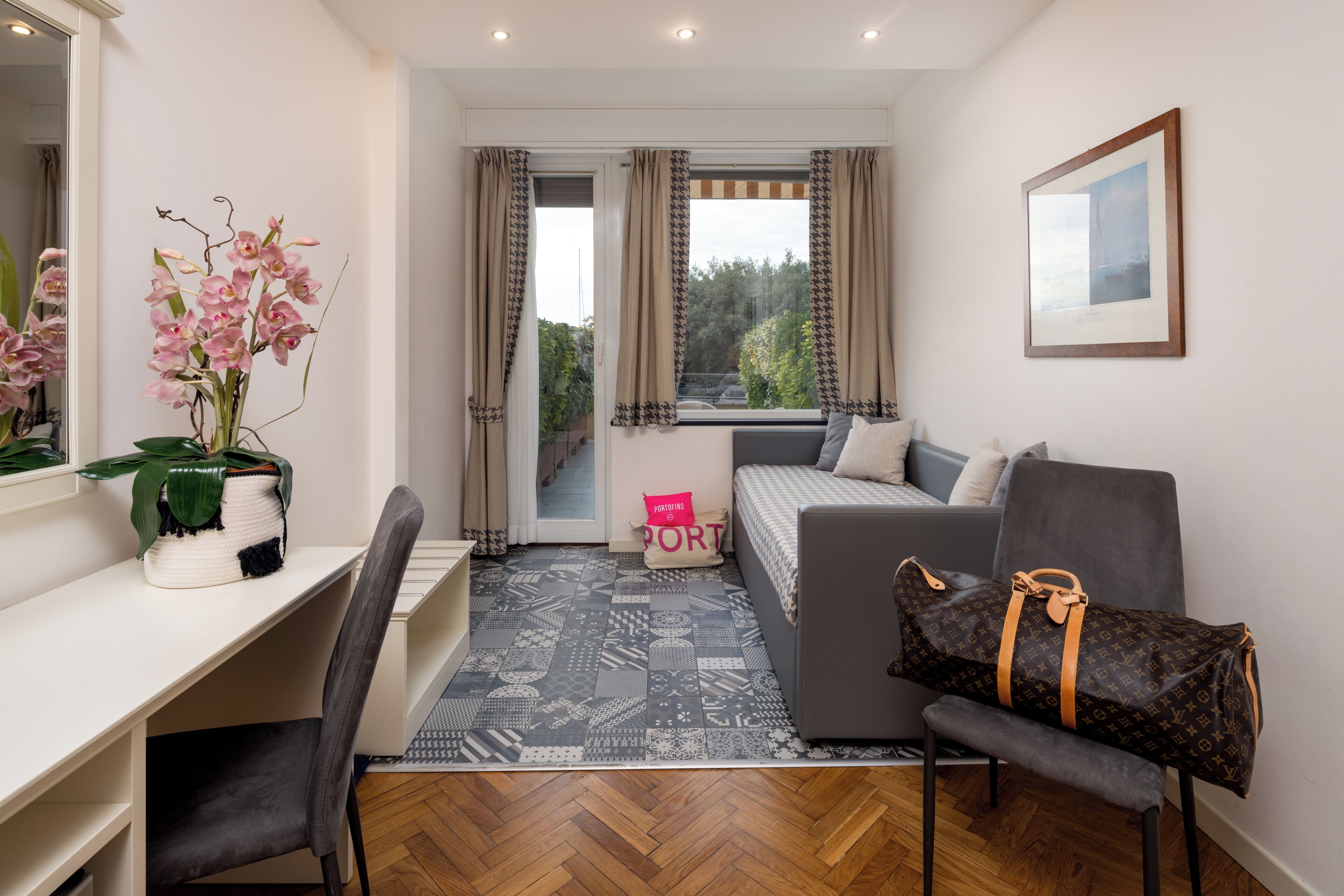 Una sala moderna con un sofá, un escritorio, una silla, un bolso Louis Vuitton y una ventana con cortinas.