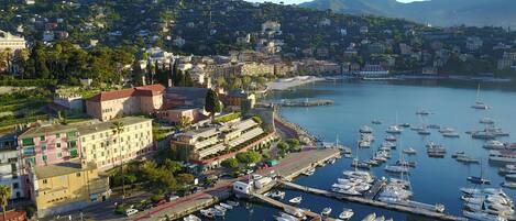 Un port de plaisance où sont amarrés de nombreux bateaux, entouré d’une ville côtière avec ses bâtiments et dominé par des collines en arrière-plan.