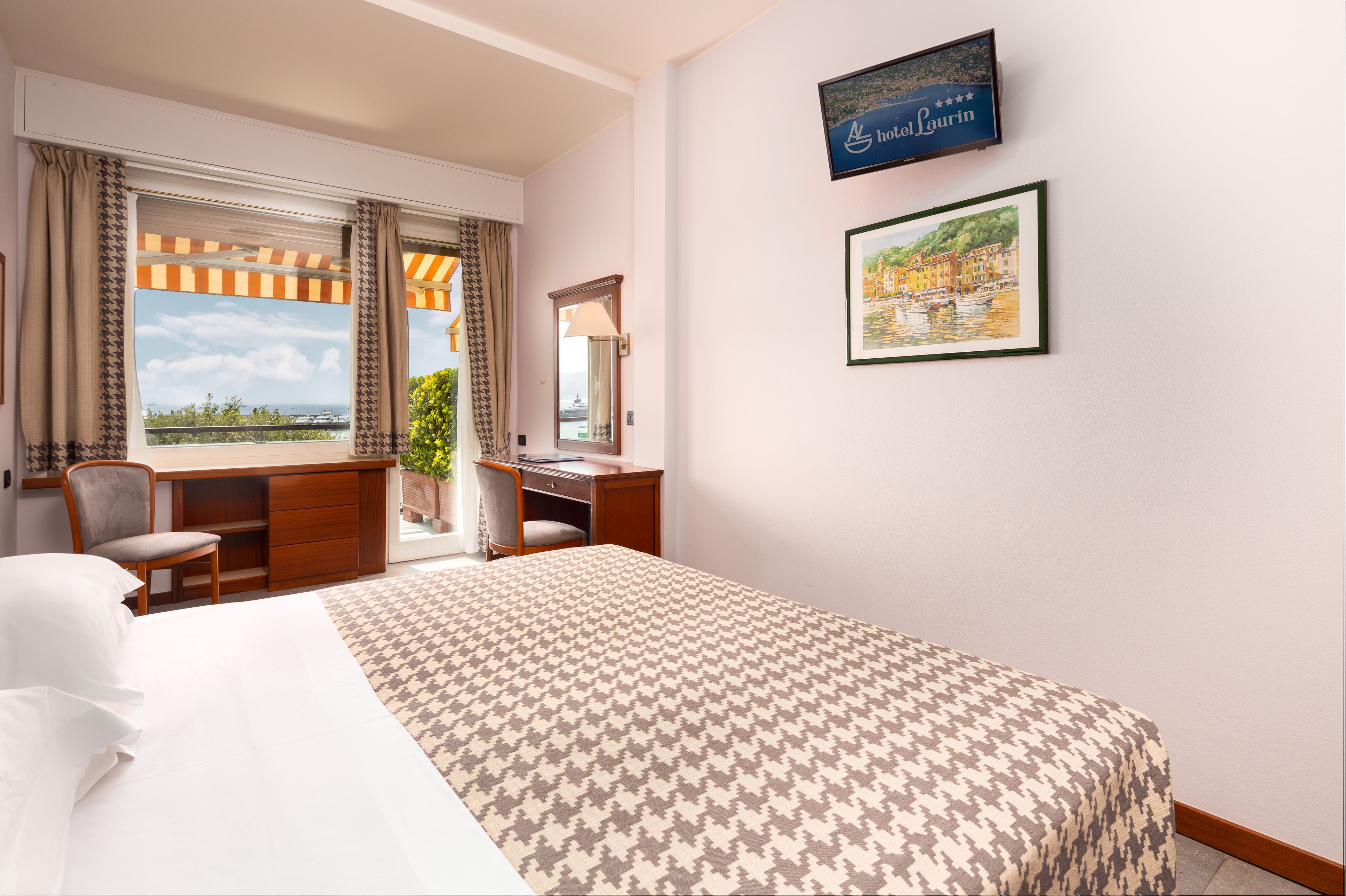 A hotel room with a large bed, a desk, a chair, a window with curtains, a framed picture, and a sign on the wall.