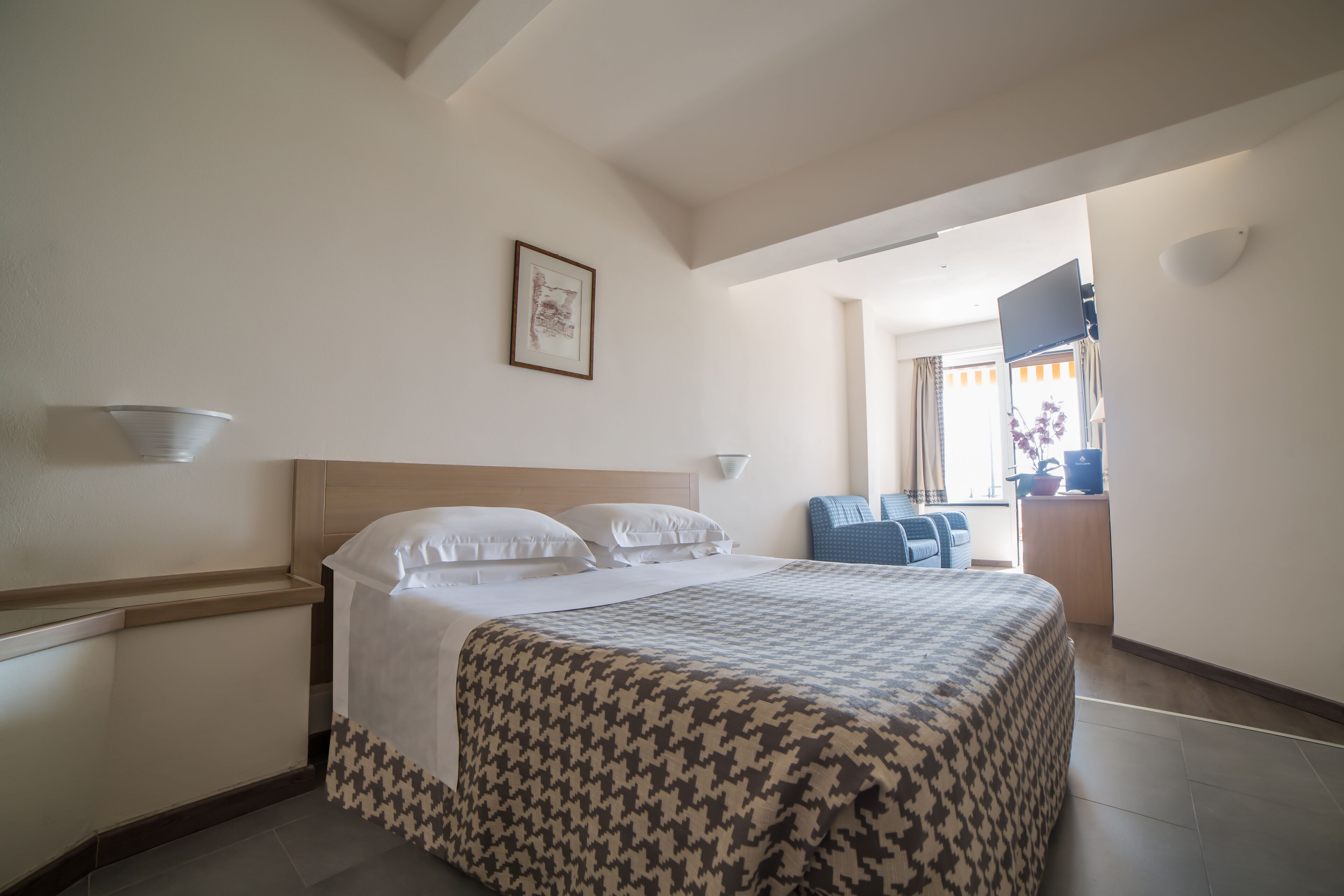 A hotel room with a bed, a desk, a chair, and a television.