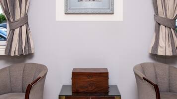 Una habitación con dos sillones, un cofre de madera y un cuadro en la pared.