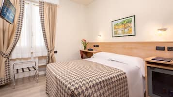 A hotel room with a bed, a desk, a chair, a TV, and a painting on the wall.