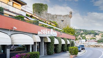 A hotel with a stone tower and a red facade, located near a curved road with parked cars.