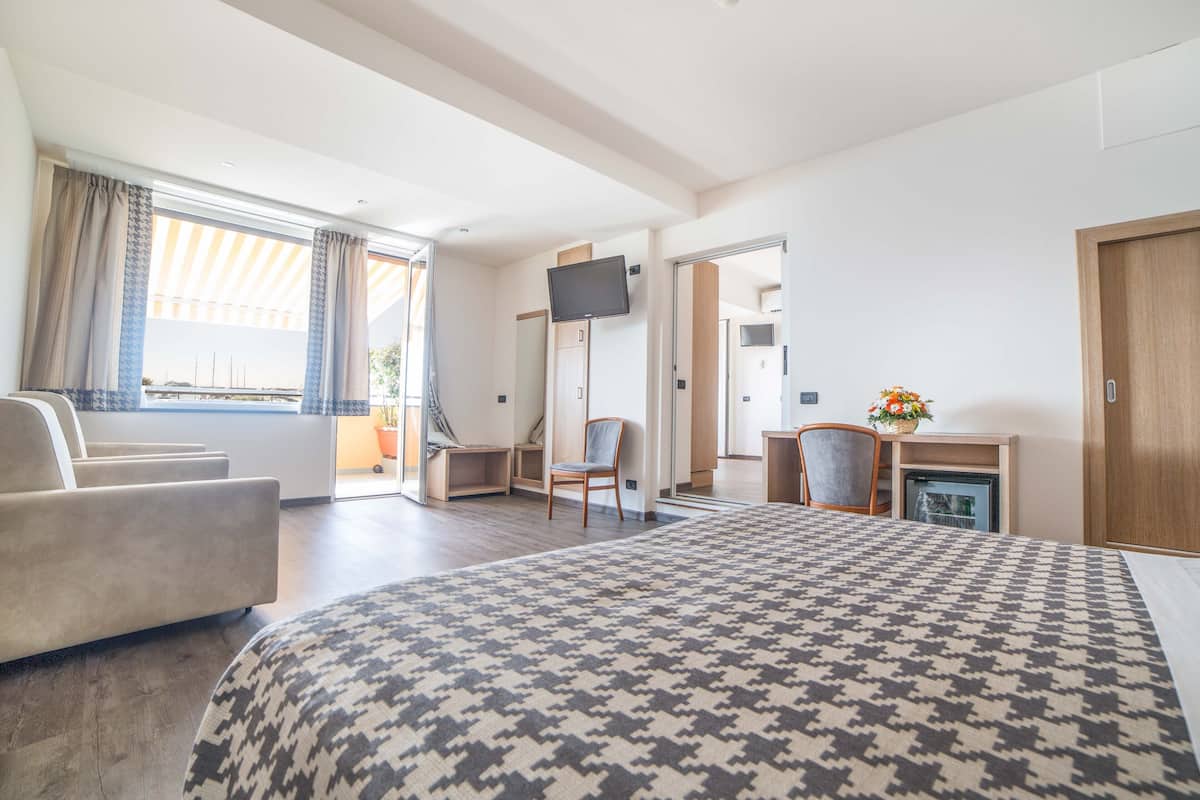 Une chambre d’hôtel avec un grand lit, un canapé, un bureau avec une chaise, une télévision et un petit réfrigérateur.