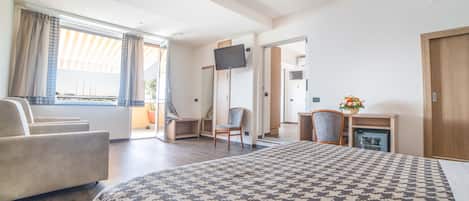 Habitación de hotel con una cama grande, un sofá, un escritorio con silla, televisor y un refrigerador pequeño.