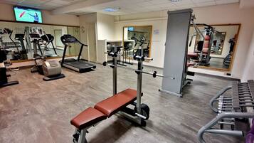 A gym with cardio machines, weightlifting equipment, and a bench.