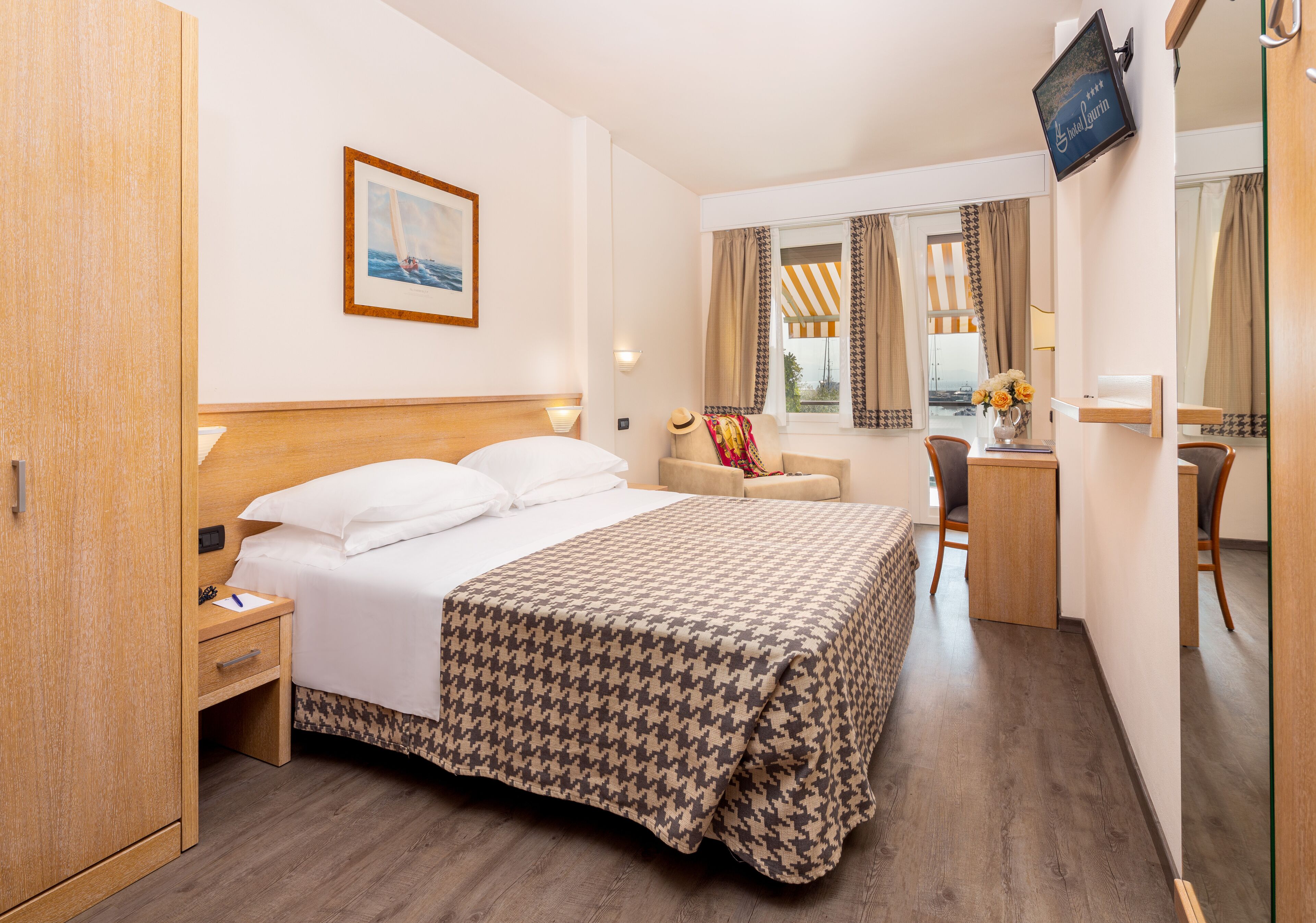 Ett hotellrum med en säng, ett skrivbord, en stol, en tv och ett fönster med gardiner.