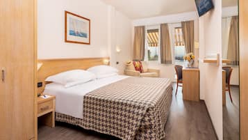 A hotel room with a bed, a desk, a chair, a TV, and a window with curtains.