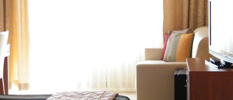 Una habitación de hotel con una cama, televisión, escritorio y sofá.