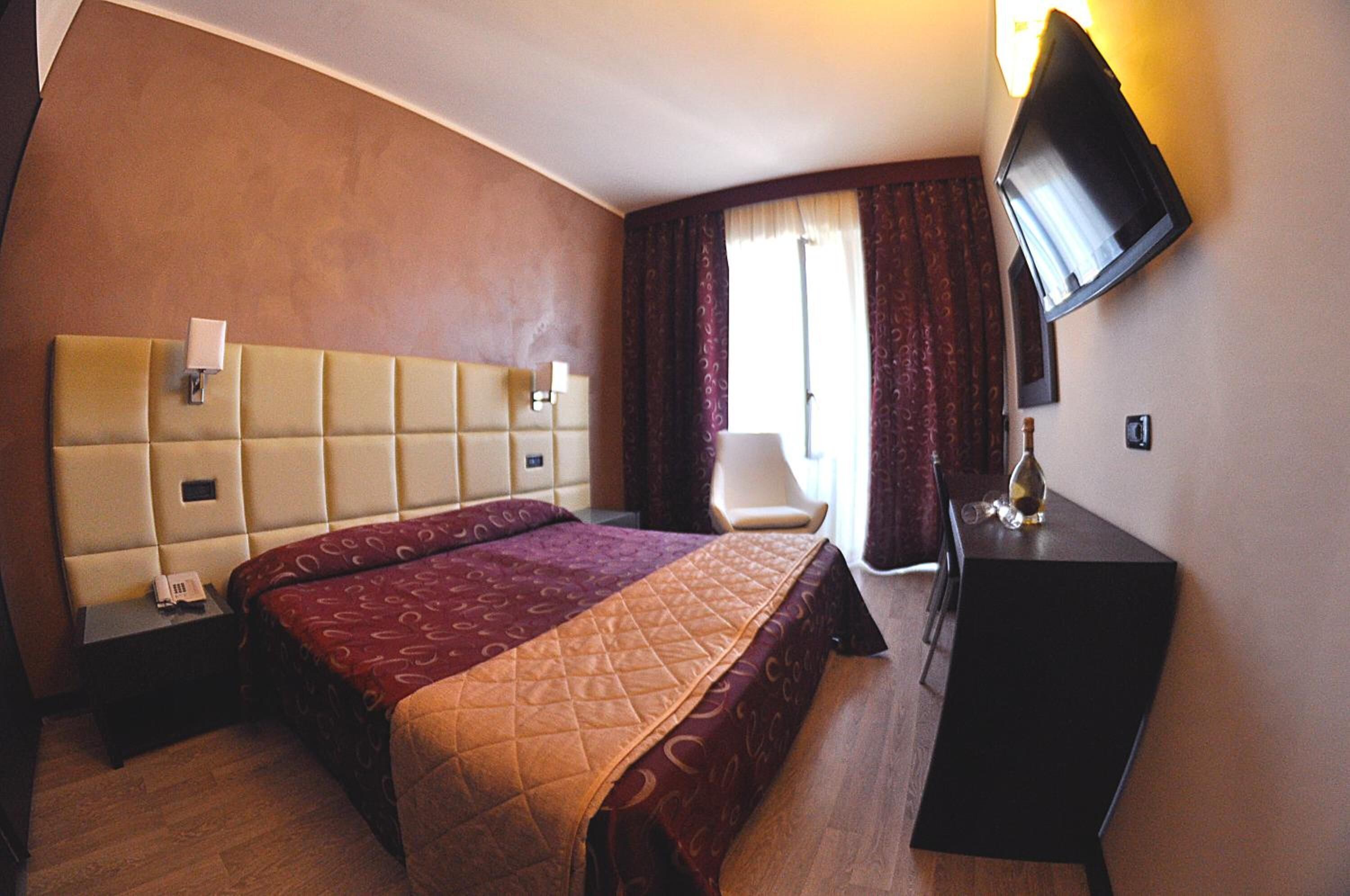 A hotel room with a large bed, a desk, a chair, a TV, and a window with curtains.