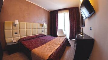 A hotel room with a large bed, a desk, a chair, a TV, and a window with curtains.