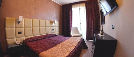 Habitación de hotel con una cama grande, un escritorio, una silla, un televisor y una ventana con cortinas.