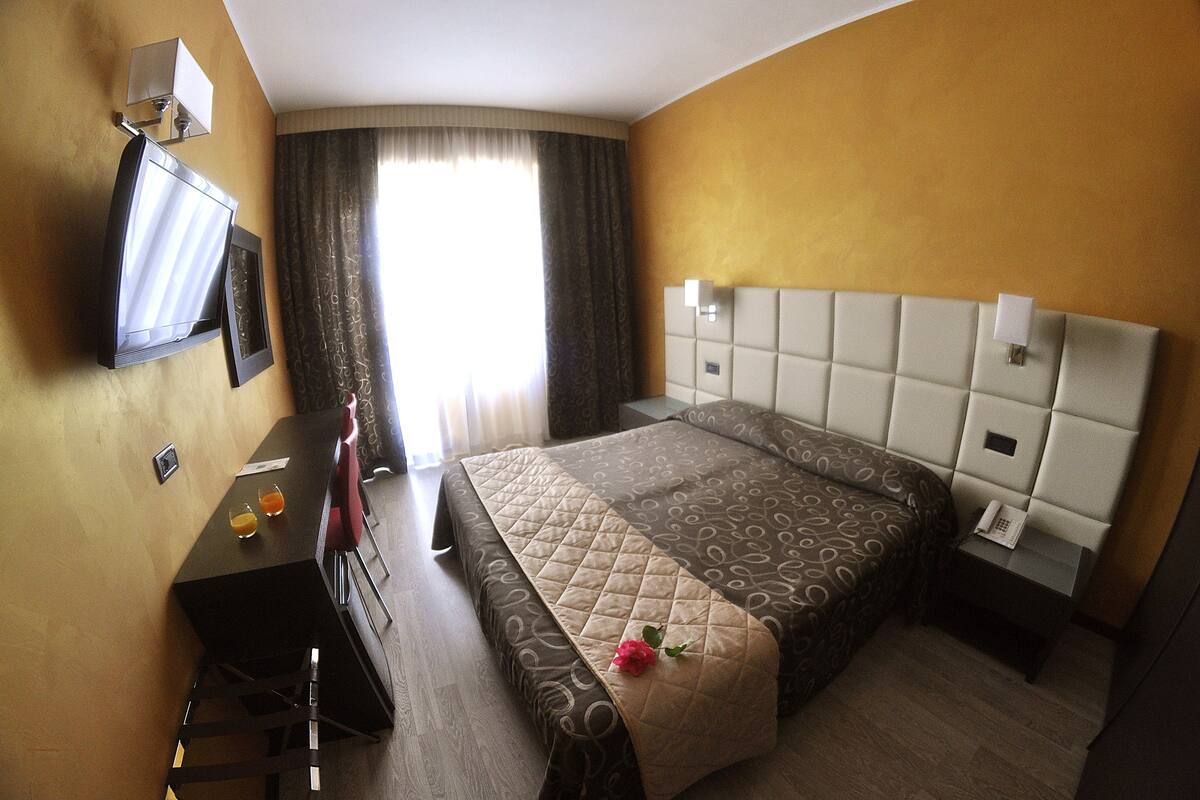 A hotel room with a bed, a desk, a chair, a TV, and a window with curtains.