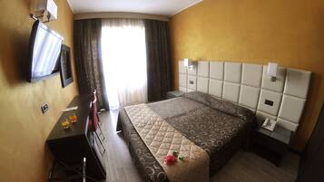 Ein Hotelzimmer mit Bett, Schreibtisch, Stuhl, Fernseher und einem Fenster mit Vorhängen.