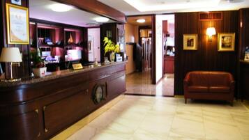 Eine Hotelhalle mit einer Rezeption, einem Ledersofa und einem Gang zu weiteren Bereichen.