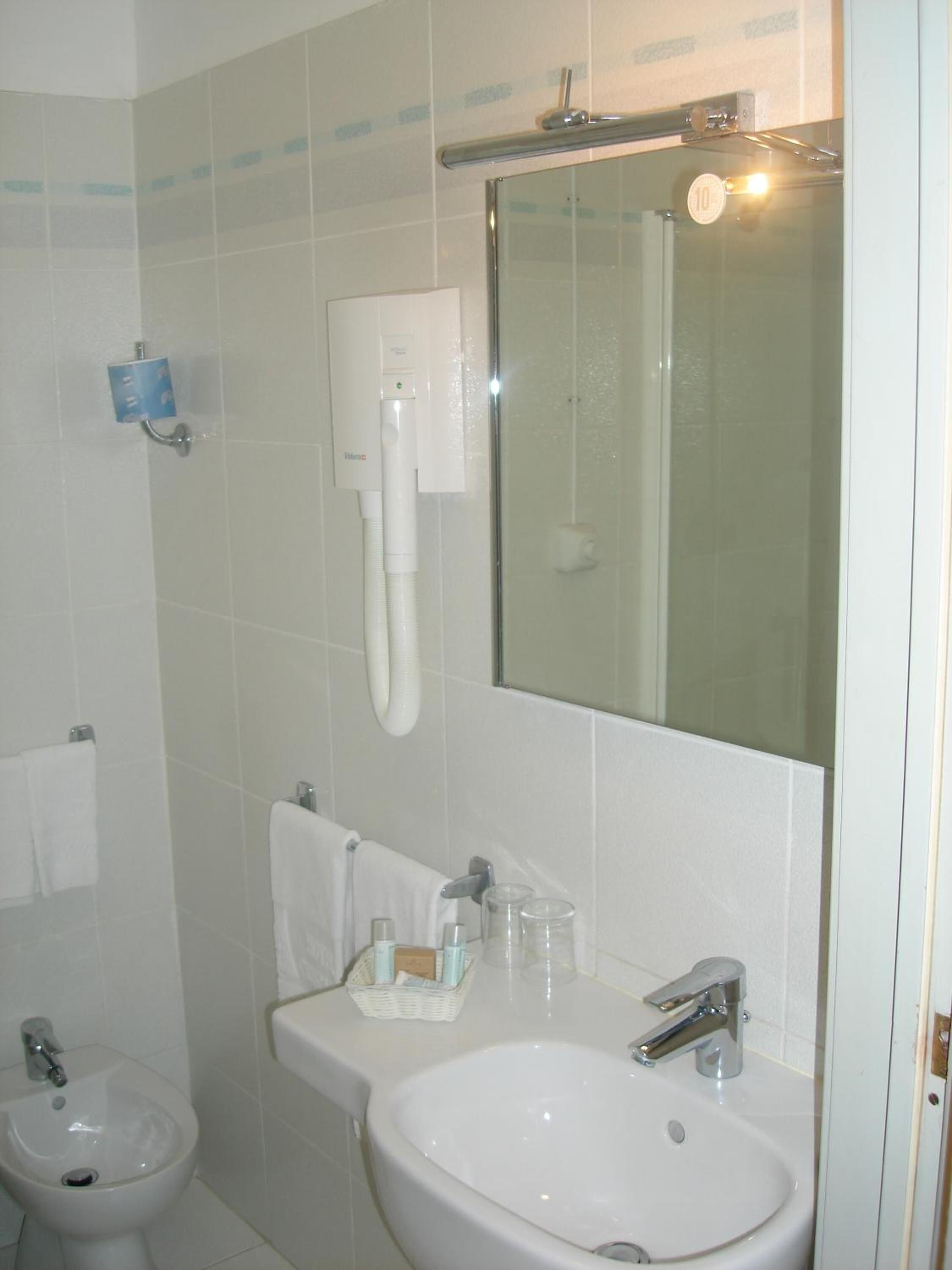 A bathroom with a white sink, a bidet, a mirror, and a towel rack.