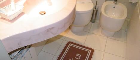 Un bagno con lavandino, water, bidet e un tappetino con il nome dell'hotel.