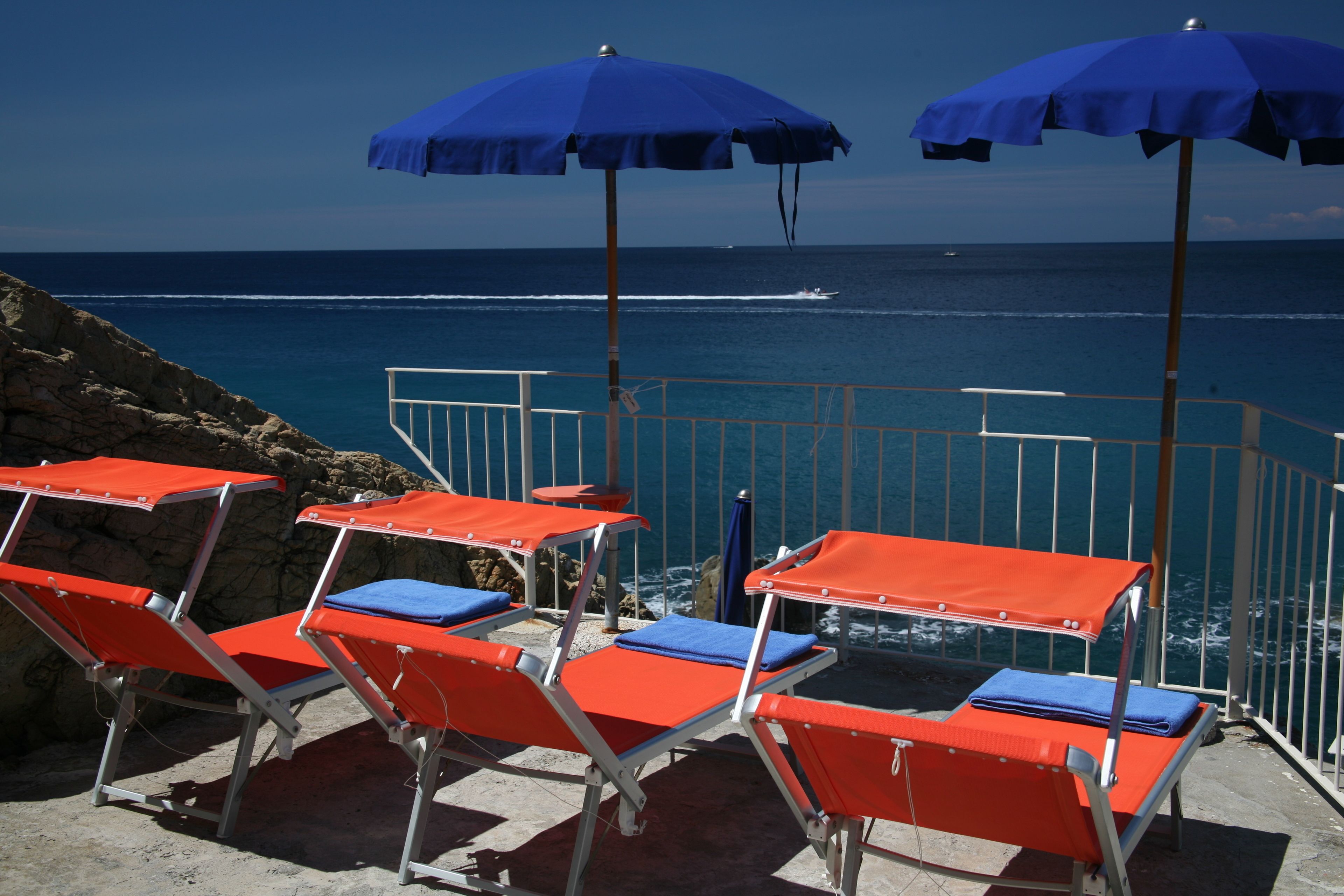 Sillas de playa con cojines azules y cubiertas rojas, dispuestas sobre una terraza de hormigón con vista al océano.