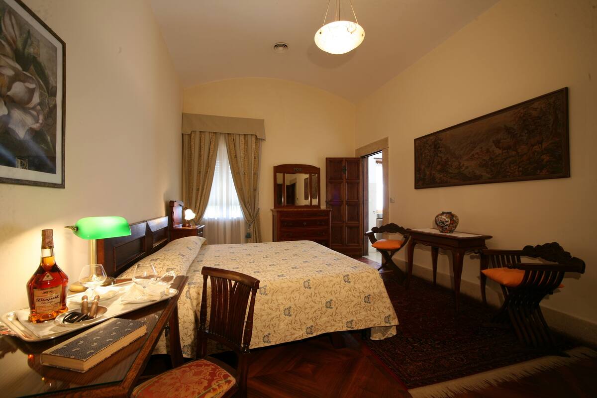 Ein Hotelzimmer mit Bett, Schreibtisch mit Lampe, Stuhl, Kommode und einem Bild an der Wand.