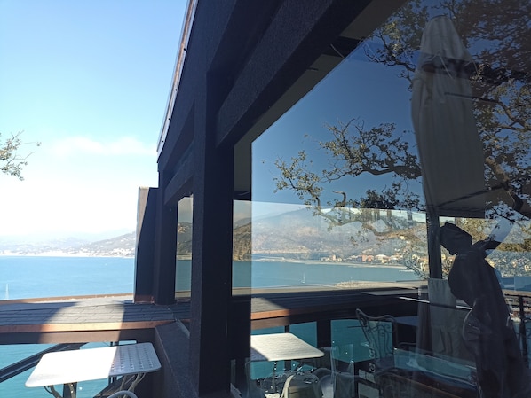 A terrace with a view of the sea and mountains, featuring a table and chairs, and a statue.