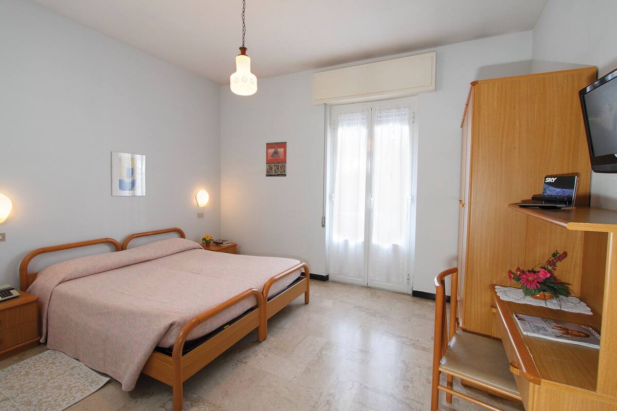 A bedroom with a bed, bedside tables, a desk with a chair, a TV, and a window with curtains.