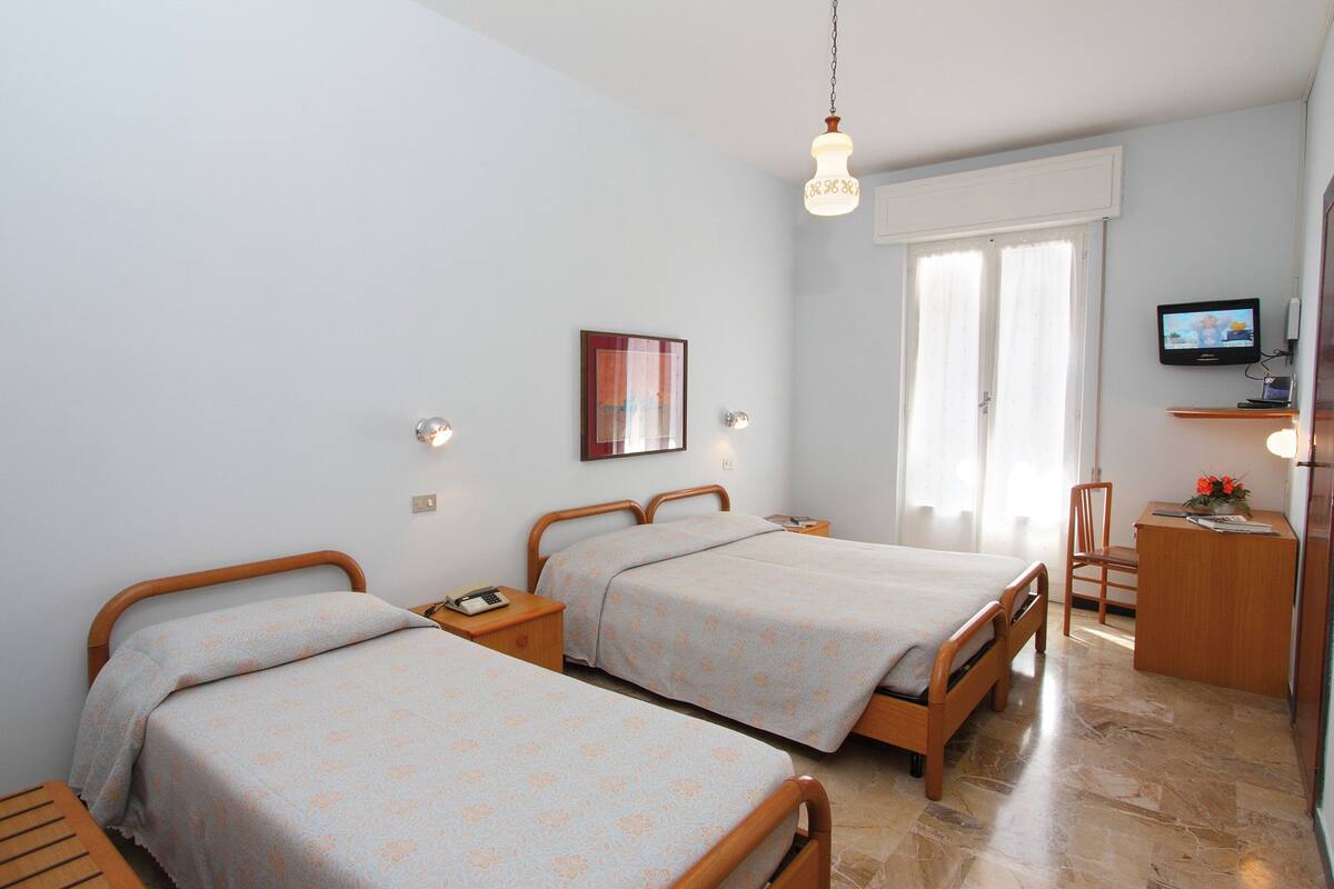 A hotel room with two beds, a desk, a chair, a TV, and a window with curtains.