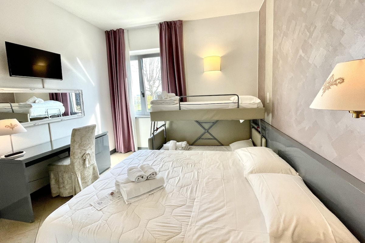 A hotel room with a bed, a desk, a chair, a television, and a window with curtains.