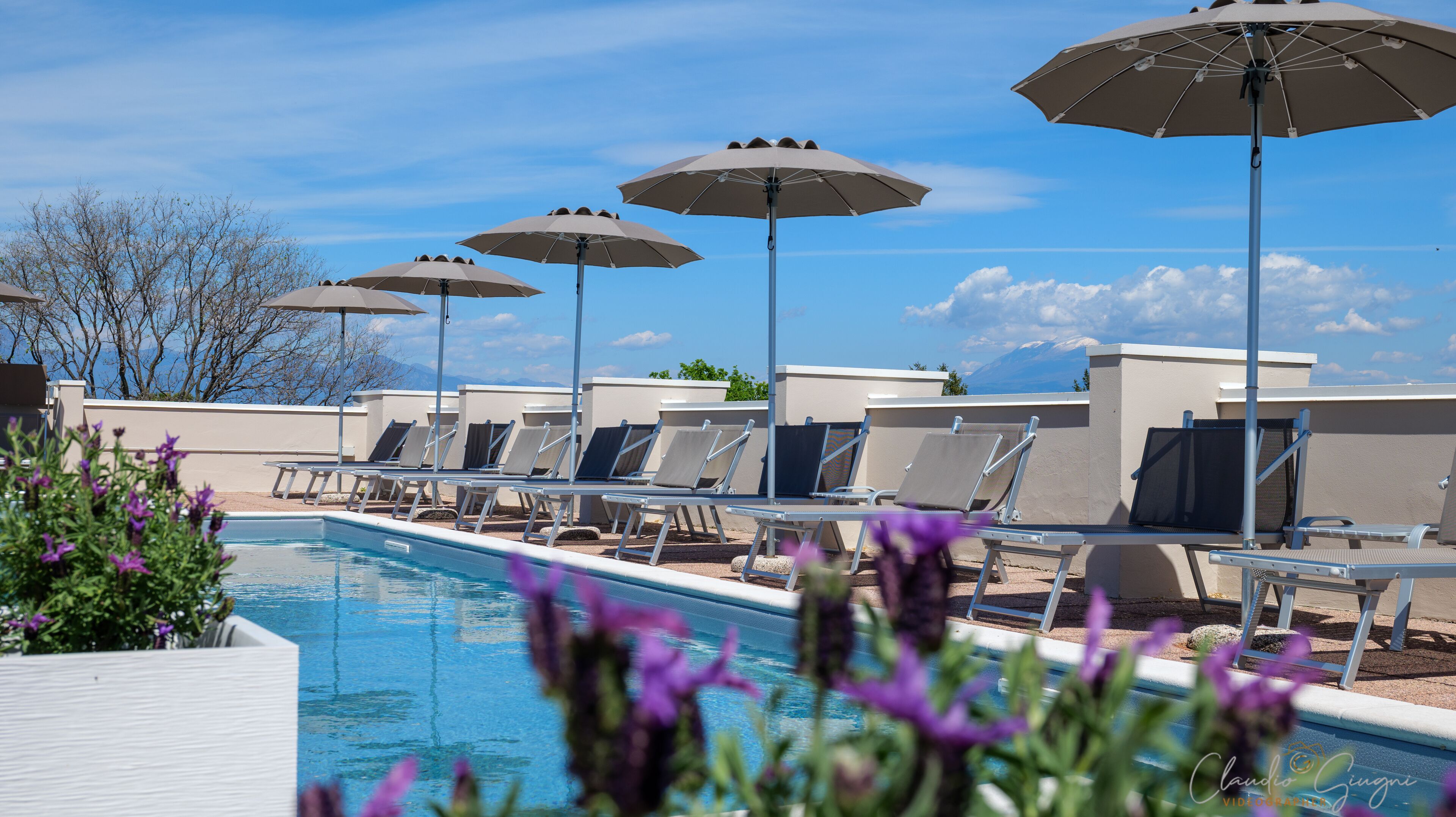 Ein Poolbereich mit Liegestühlen und Sonnenschirmen, bewölkter Himmel und Blick auf die Berge.